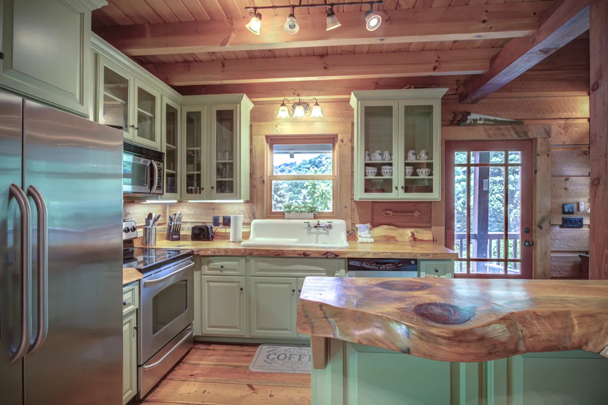 A spacious kitchen featuring a large wooden countertop, modern stainless steel appliances, cabinets with glass doors filled with dishes, and a window offering an inviting view. The room is warmly lit and arranged for easy movement and convenient access to all cooking essentials, creating a homely, functional cooking environment.
