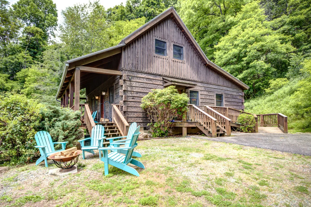 The hero image showcases a charming wooden cabin surrounded by lush greenery. Adirondack chairs are arranged around a crackling fire pit, inviting guests to gather and relax outdoors. The porch offers a vantage point for breathtaking mountain sunsets, and the tranquil yard stands ready for morning coffee or evening stargazing.