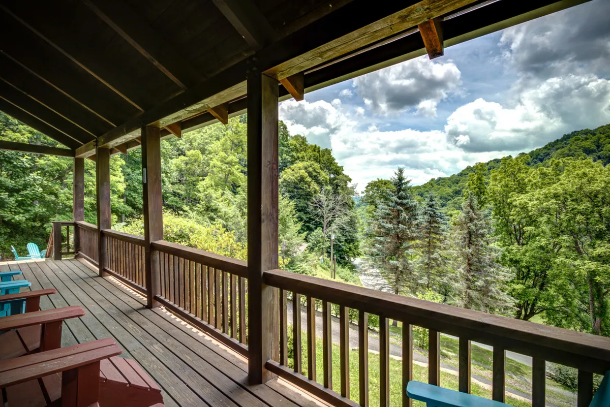 A wooden deck is shown with blue Adirondack chairs positioned to face a panoramic mountain view. The setting is serene and inviting, ideal for gatherings, relaxation, or simply appreciating nature. The spaciousness and outdoor accessibility suggest a welcoming spot for both pets and their owners to explore and play.