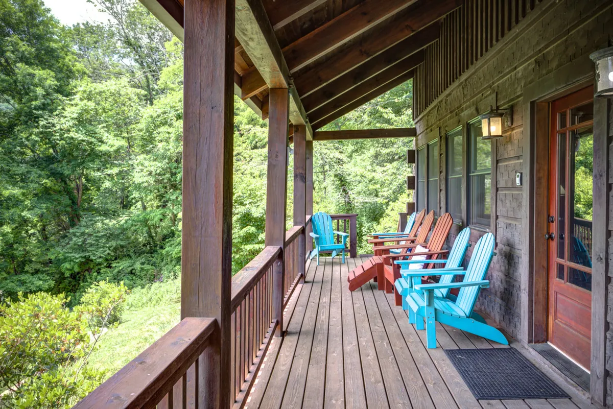 A tranquil scene with colorful Adirondack chairs arranged on a wooden deck, framed by lush greenery and a sturdy railing. The chairs face outward, inviting guests to relax, watch wildlife, or gaze at the stars, set against the backdrop of the surrounding forest.