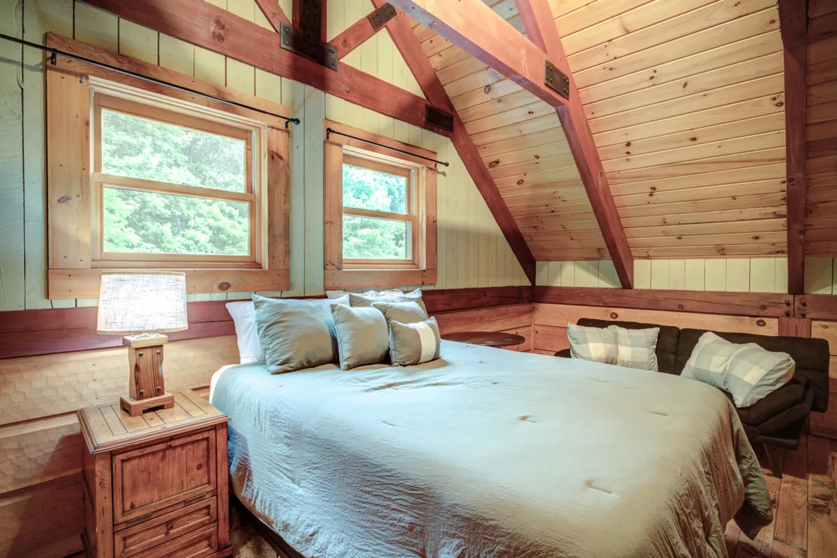 This image features a cozy bedroom with a large bed, nightstand, ample windows inviting in natural light, and a nearby sofa. The arrangement and details suggest a restful, comfortable atmosphere ideal for relaxation and privacy.