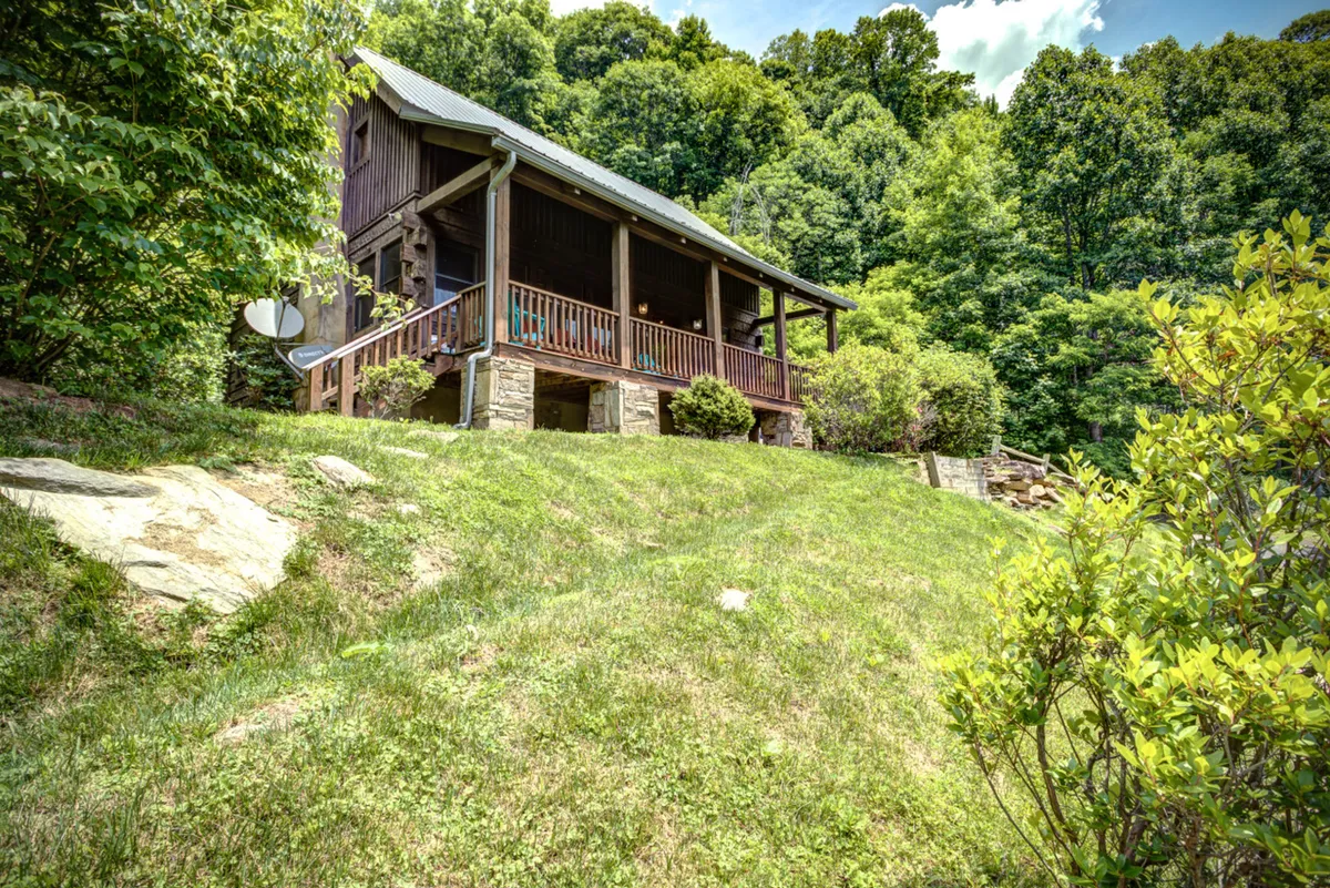 This image shows the wooden porch of the Cozy Mountain Cottage, highlighted by a sturdy stone foundation and surrounded by lush greenery. The inviting porch is bathed in natural light and offers scenic views of the surrounding landscape, hinting at the mountains and adventures beyond.