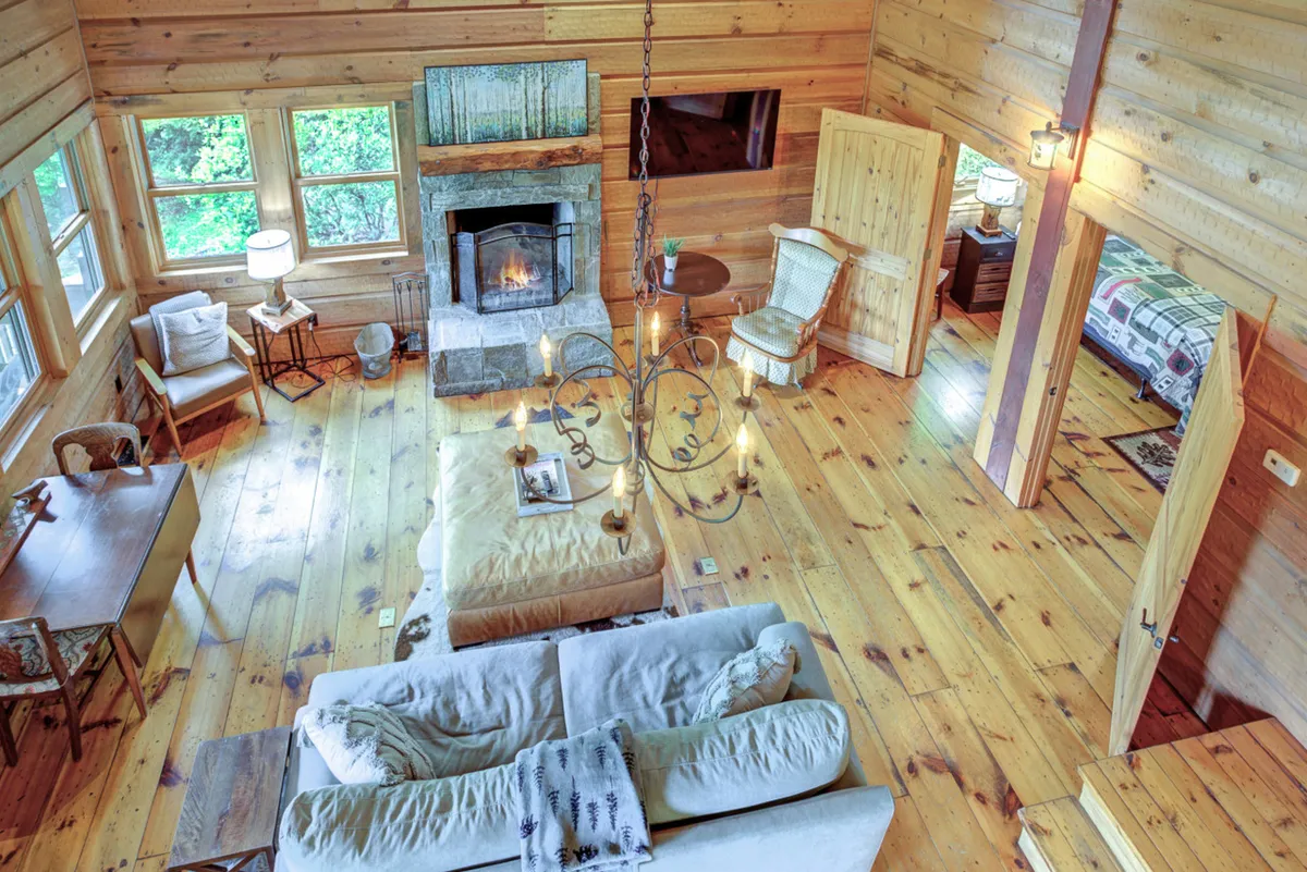 A beautifully styled interior showing a living space that flows seamlessly into the dining area. Features include a central fireplace, a plush sofa, a dining table, and a chandelier, all bathed in warm light from nearby windows. The inviting setting is ideal for both casual relaxation and lively gatherings.