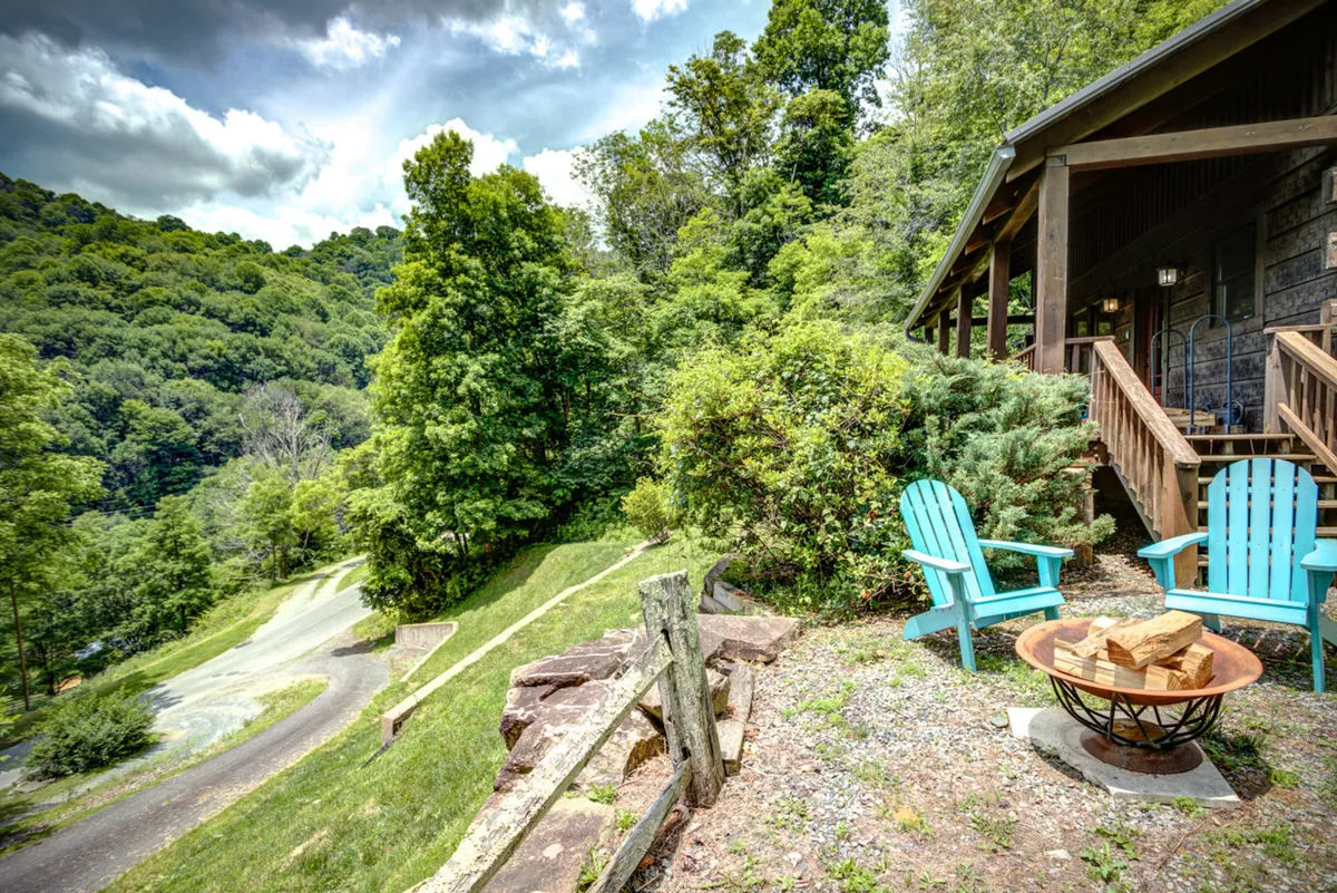 This image shows a set of Adirondack chairs gathered around a fire pit in an open outdoor space. The landscape view beyond features rolling greenery and hints of mountains, capturing the tranquil, natural setting. The space is ideal for relaxing, socializing, and enjoying the outdoors with both human and canine companions.