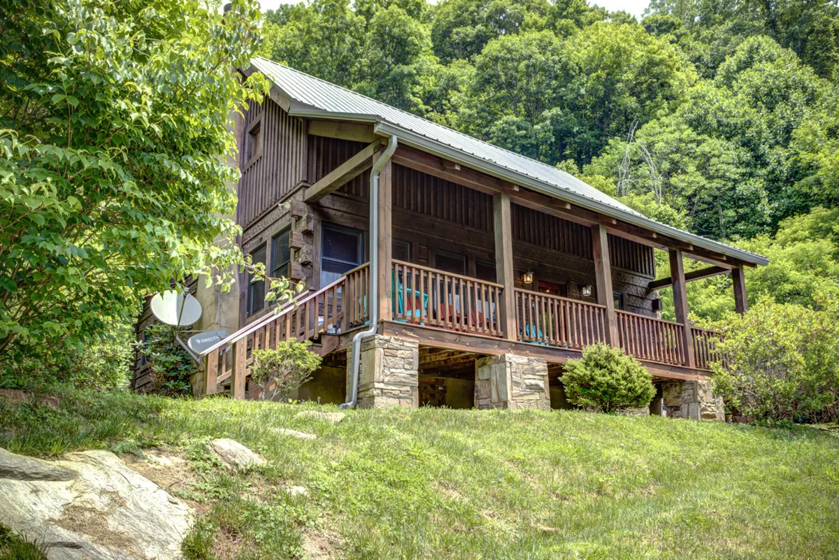 A welcoming wooden porch with a sturdy stone base, surrounded by lush greenery. The space is furnished for relaxation and opens directly onto the yard, offering views ideal for enjoying morning coffee or evening gatherings. The porch is covered, making it usable in all weather and providing a seamless transition from indoors to outdoors.