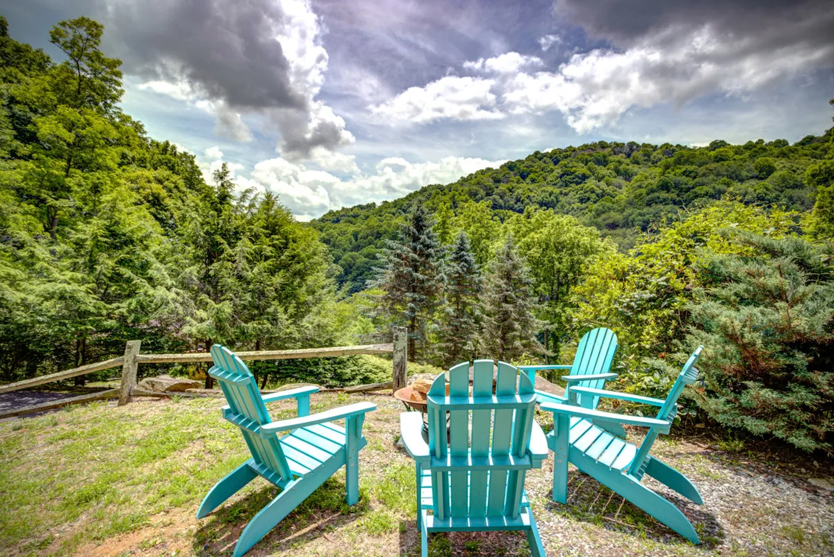 An inviting outdoor setup features Adirondack chairs gathered around a fire pit, with panoramic mountain views in the background. The space is designed for couples to unwind, share stories, or stargaze under the night sky.