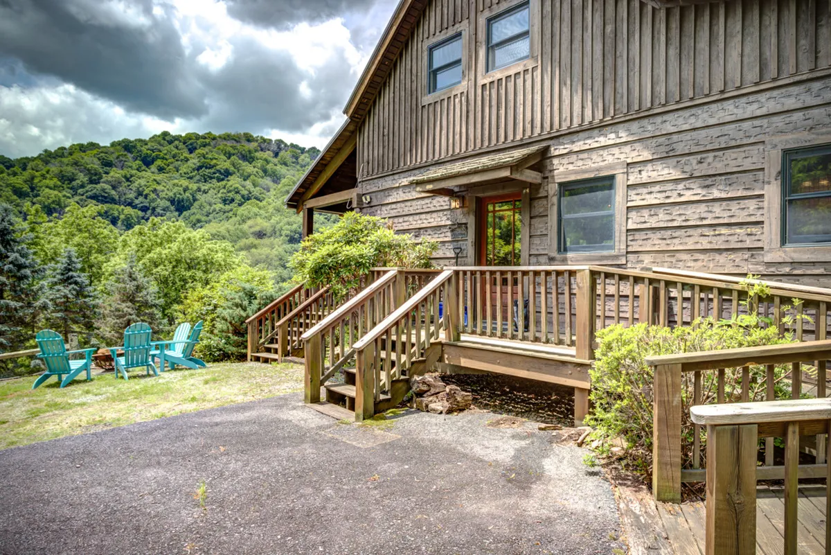 The image features a wooden deck with green Adirondack chairs, surrounded by trees and overlooking a beautiful mountain view. The expansive deck area offers ample space for relaxation, outdoor activities, and soaking in scenic vistas. The peaceful, natural environment is highlighted by the connection between the deck and the surrounding landscape.