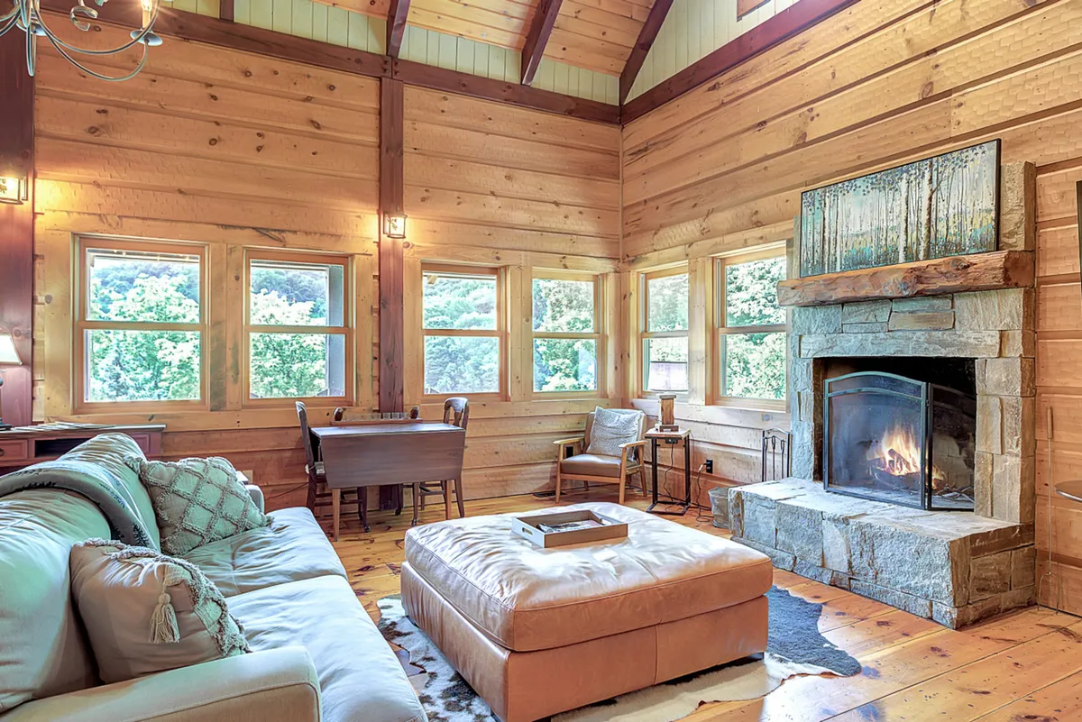 A welcoming living room featuring a fireplace, expansive windows framing mountain views, a comfy sofa, and a coffee table. The space is filled with natural light, and the arrangement encourages relaxed conversations, reading, or simply enjoying the view.