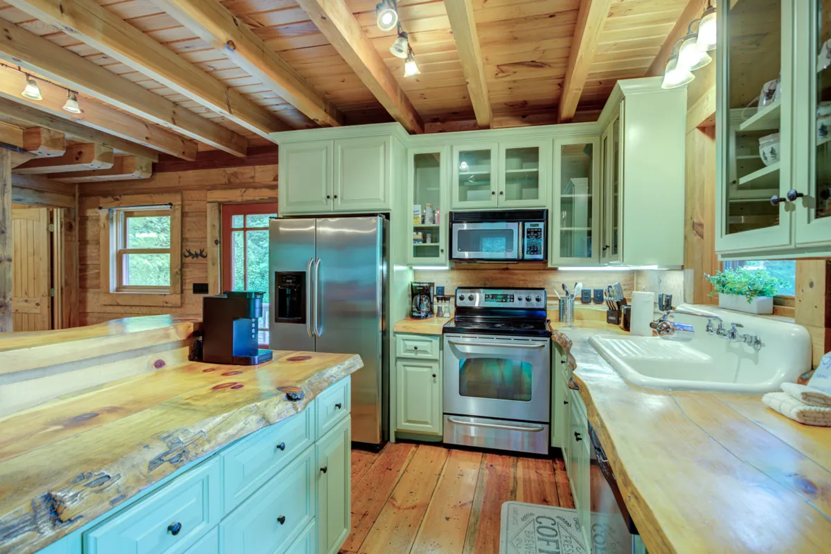 A cozy kitchen space with wooden countertops, open shelving stocked with cookware and spices, stainless steel appliances, and a large sink. The open layout allows a seamless view into the adjacent living space, emphasizing the communal aspect of the kitchen.