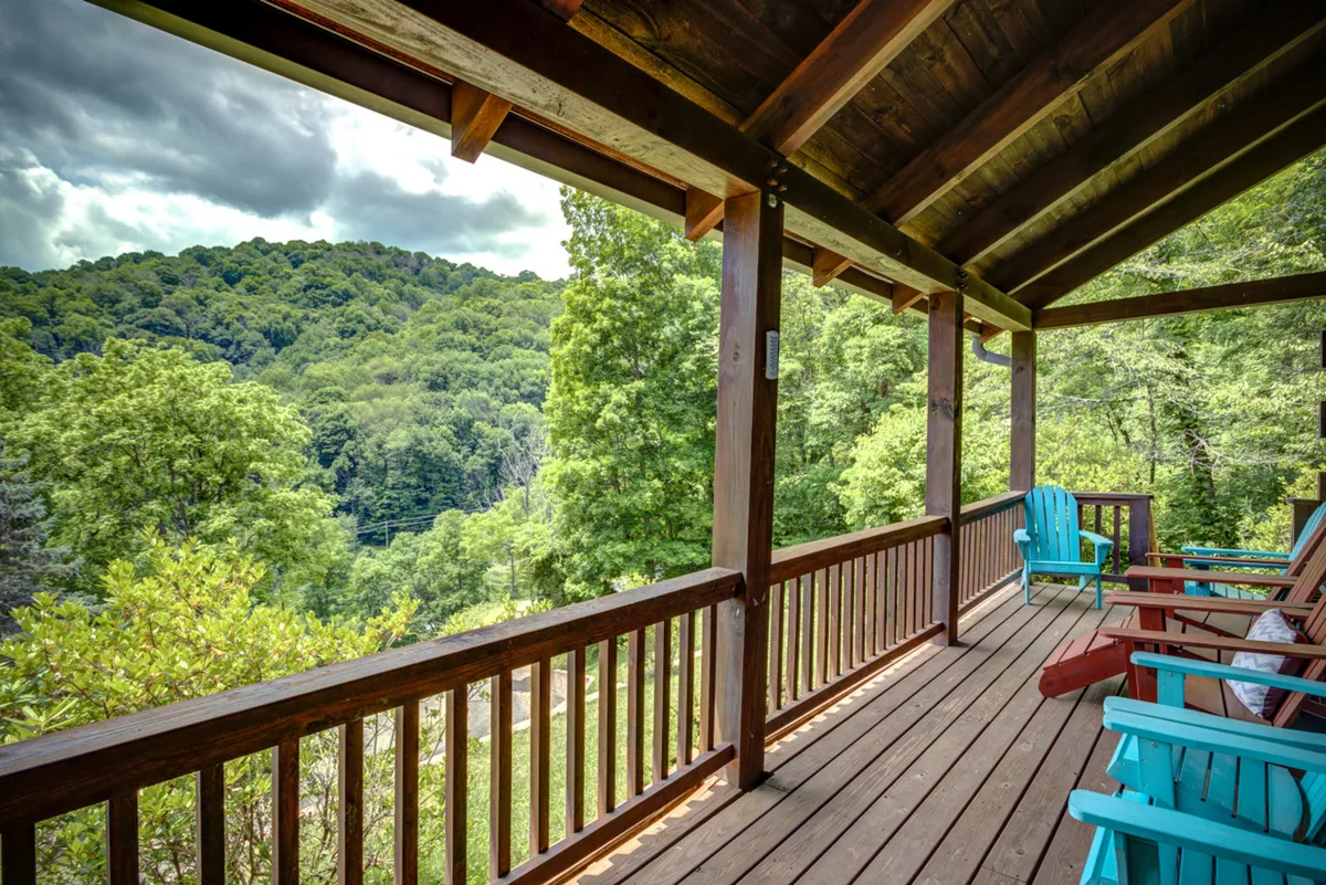 A peaceful wooden deck furnished with colorful chairs overlooks expansive mountain views, with surrounding trees framing the scene. The area is perfect for couples to relax and take in the natural beauty, making it ideal for morning coffee or sunset conversations.